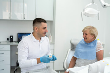 Obraz premium dentist consulting a retired woman with the installation of a tooth crown, an implant. Artificial teeth with steel pin
