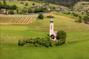 Chiesa di San Valentino with tree lines on Seiser Alm, Dolomites, aerial view. Rural chapel within the alpine landscape