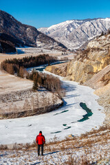Winter landscape in Siberia, Russia. Katun river and Altai mountains with a male tourist in red jacket. Altai Republic, Russia