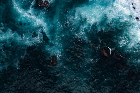 Turbulent ocean water around volcanic reefs and boulders, top down view