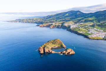 Obraz premium Volcanic islet lagoon with shallow sandy area and rock walls near Azorean coastline, drone view