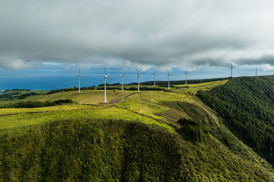 Wind turbines on green volcanic hills of Sao Miguel Island under variable clouds. Renewable energy production supporting energy transition