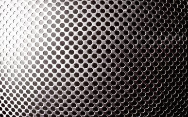 Primer plano de superficie oscura perforada con orificios circulares uniformes y reflejos brillantes sutiles.Rejilla de frontal de altavoz