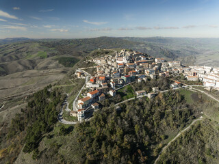 Aerial view of the compact hilltop town with aged buildings casting shadows on winding roads, surrounded by the undulating green hills, Cairano, Irpinia, Campania, Italy.