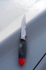 Serrated knife with black handle and red tip placed on light surface.
