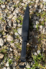 Black knife sheath with belt loop placed on gravel with grass patches.