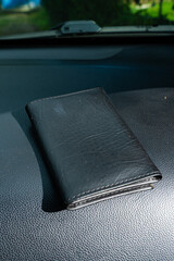 Black leather wallet placed on car dashboard with outdoor background.