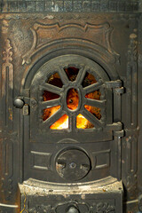 Cast iron wood burning stove door with visible fire flame behind metal grate. Indoor heating appliance close up photography. Home heating and solid fuel stove concept.