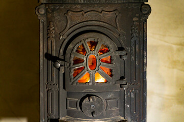 Cast iron wood burning stove door with visible fire flame behind metal grate. Indoor heating appliance close up photography. Home heating and solid fuel stove concept.