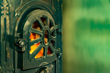 Cast iron wood burning stove door with visible fire flame behind metal grate. Indoor heating appliance close up photography. Home heating and solid fuel stove concept. Design for poster, banner