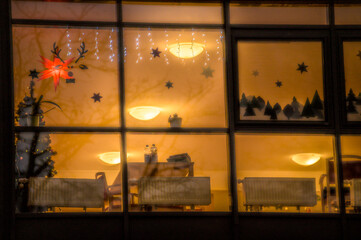 Untersicht weihnachtlich beleuchteter Versammlungsraum mit Papierstern, Lichtgirlanden und Deckenleuchten hinter Sprossenfenster in Neckartenzlingen.