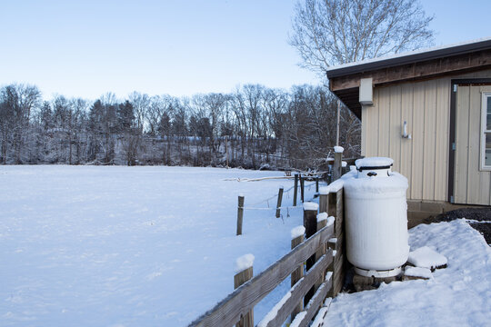 A silent snowy field and propane tanks by the fence and barn