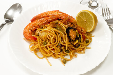 Gourmet seafood spaghetti with shrimp and mussels served on a white plate with lemon, bread and red wine. Elegant Italian Mediterranean cuisine in studio setting.