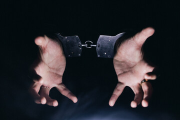 Obraz premium Hands in handcuffs are raised against a dark background, symbolizing restraint and captivity, evoking themes of justice, freedom, and the struggle against oppression
