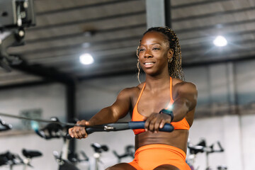 Determined black woman training on rowing machine in gym