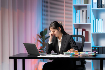 Business struggles: a thoughtful business woman works in her office surrounded by files, showing her challenges. 