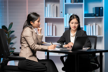 Focused Collaboration: Two business women meticulously analyze data and strategies in a well-lit office, embodying professionalism and dedication.