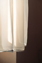 Sheer curtain gracefully drapes in soft light, casting gentle shadows on a neutral wall, enhancing the ambiance of a peaceful indoor space, ideal for home decor or interior design projects.