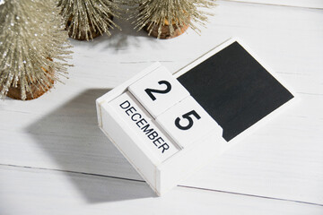 Decorative Christmas trees on a gray background and a wooden calendar with the date December 25