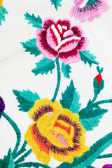 Colorful floral embroidery on cotton fabric with floral patterns on a white background. Close-up.