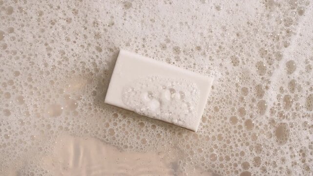 A bar of soap on a water surface with bubbles of white soapy foam. Concept of bath products, skin care products advertisement spa cosmetics. Body care and relaxation. High quality 4k footage
