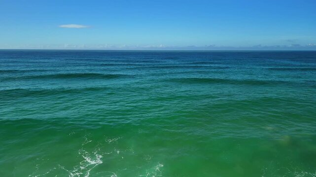 Aerial drone flight over the Atlantic coast of Portugal, moving forward above the ocean before flying backward as the camera tilts down to reveal textured waves and coastal water patterns
