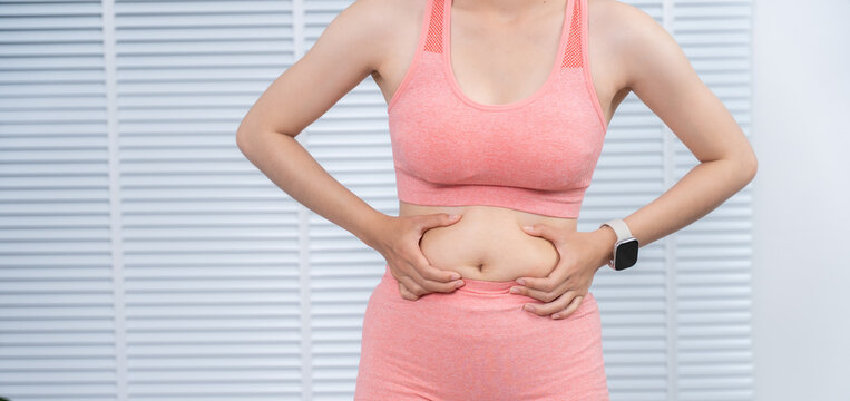 Self-Assessment: A woman examining her abdominal area in athletic attire, focusing on her body's natural state, showcasing both physical health and self-awareness.