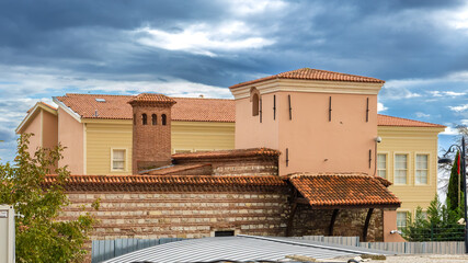 Exterior view of a historic mediterranean style building with tiled roofs, stone masonry, and pastel walls under a dramatic cloudy sky, showcasing traditional architecture and heritage design.