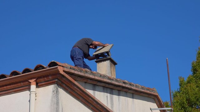 A chimney sweep on a roof reinstall cap of chimney after work