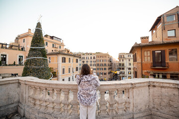 Woman enjoying a festive winter panorama overlooking Rome near the Spanish Steps with a decorated Christmas tree and historic buildings. Holiday atmosphere, winter tourism, city break travel and