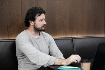 Young curly haired man working on a laptop in a modern coworking space. Remote work, freelance...