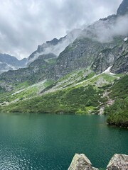 Mountain Lake Morskie Oko in Tatra Mountains, Poland. Emerald mountain lake surrounded by rocky Tatra Mountains with misty clouds and green slopes in Poland. © Iryna