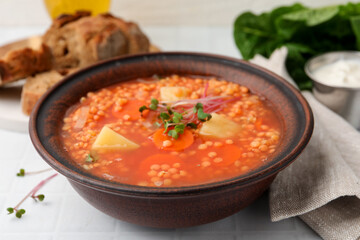 Tasty lentil soup in bowl on white tiled table, closeup