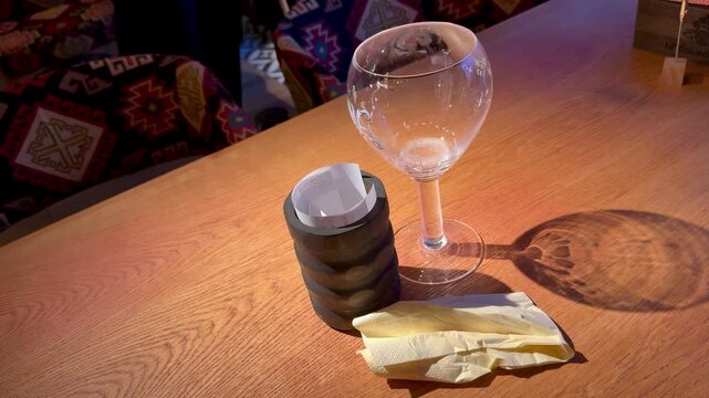 Wine glass stacked cookies wafer on wooden table, warm amber lighting casts elongated shadow, patterned upholstery background, clear glass reflection and rustic texture create