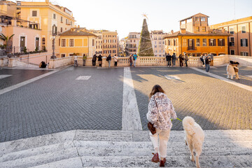 Woman walking with a dog toward a festive square in Rome near the Spanish Steps. Holiday atmosphere, winter tourism, city break, New Year celebration, joyful travel, freedom and European lifestyle