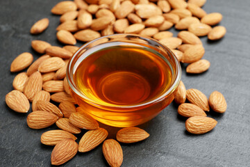 Delicious honey in glass bowl and almonds on dark textured table, closeup