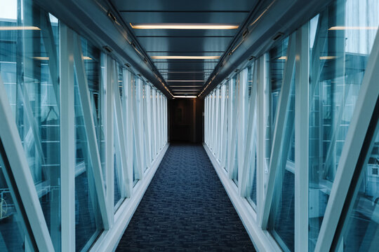 Airport jet bridge corridor interior. Long glass walkway perspective. Empty passenger boarding tunnel. Modern terminal architecture design. Symmetry lines and vanishing point. Travel concept.
