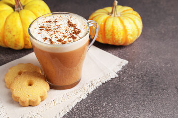 Delicious pumpkin latte in glass cup, cookies and fresh vegetables on grey textured table, closeup. Space for text