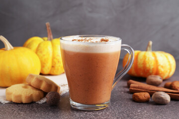 Delicious pumpkin latte in glass cup, spices, cookies and fresh vegetables on grey textured table, closeup