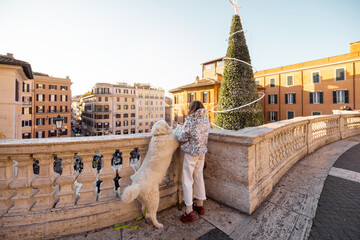 Woman with her dog enjoying a festive winter moment overlooking Rome near the Spanish Steps with a decorated Christmas tree. Holiday atmosphere, winter tourism, city break travel, joy, togetherness