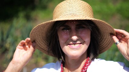 Portrait of happy ukrainian woman in traditional vyshyvanka at sunny summer day. Adult smiling lady wearing in straw hat looking into camera outdoor. Concept of national identity and patriotism
