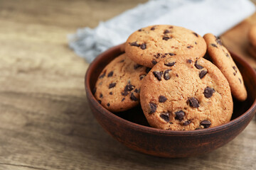 Delicious chocolate chip cookies in bowl on wooden table, closeup. Space for text