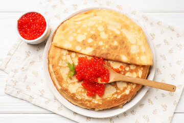 Tasty crepes with red caviar on white wooden table, flat lay
