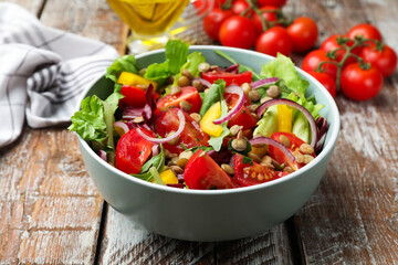 Delicious salad with lentils and vegetables in bowl on wooden table, closeup