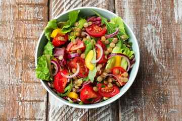 Delicious salad with lentils and vegetables in bowl on wooden table, top view