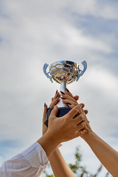 Hands raising trophy against a clear blue sky