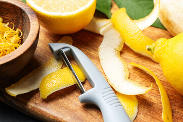 Fresh lemons with zest, peeler and leaves on table, closeup
