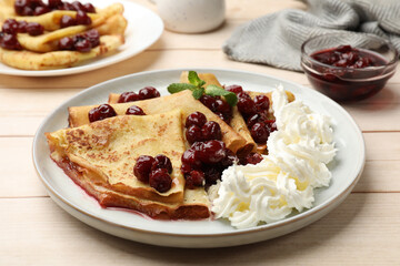 Tasty crepes with cherries, whipped cream and mint served on white wooden table, closeup