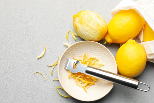 Fresh lemons with zest and zester tool on grey table, flat lay. Space for text