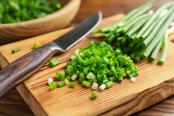 Cut green onions and knife on wooden table, closeup
